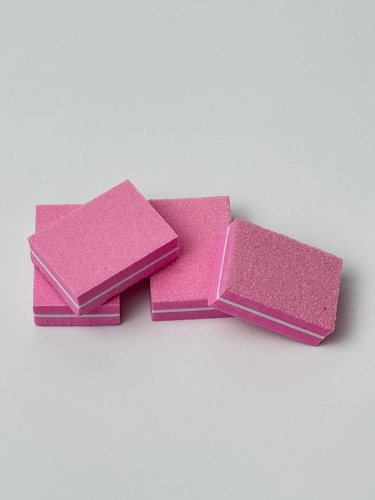 Four pink nail buffer blocks stacked on a plain background, used for smoothing and shining nails during manicure prep