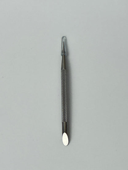 Stainless steel dual-ended cuticle pusher placed on a plain background, used for pushing back cuticles and cleaning around the nail
