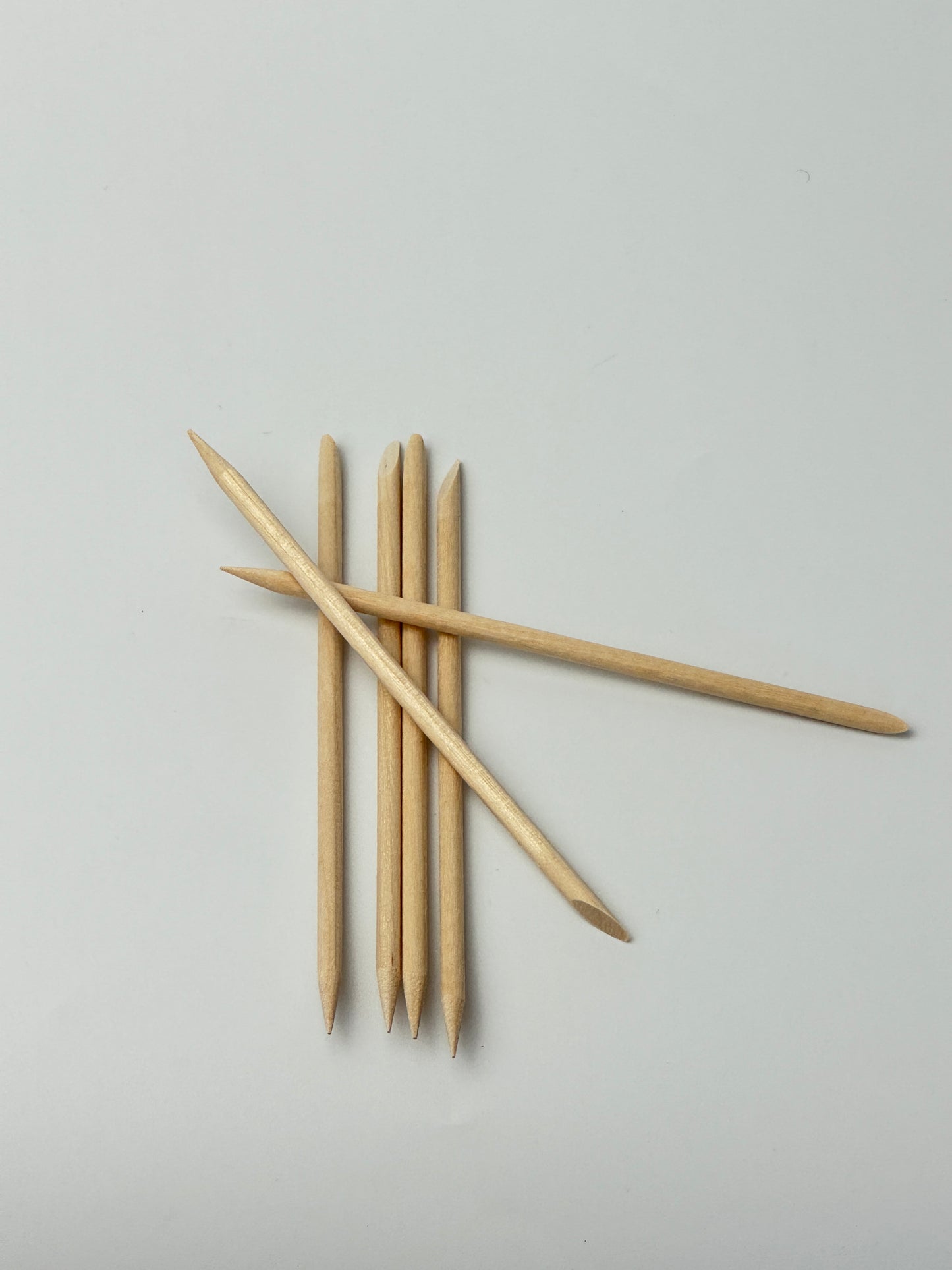 Set of double-ended wooden cuticle sticks arranged on a light background, used for pushing back cuticles and nail cleaning.